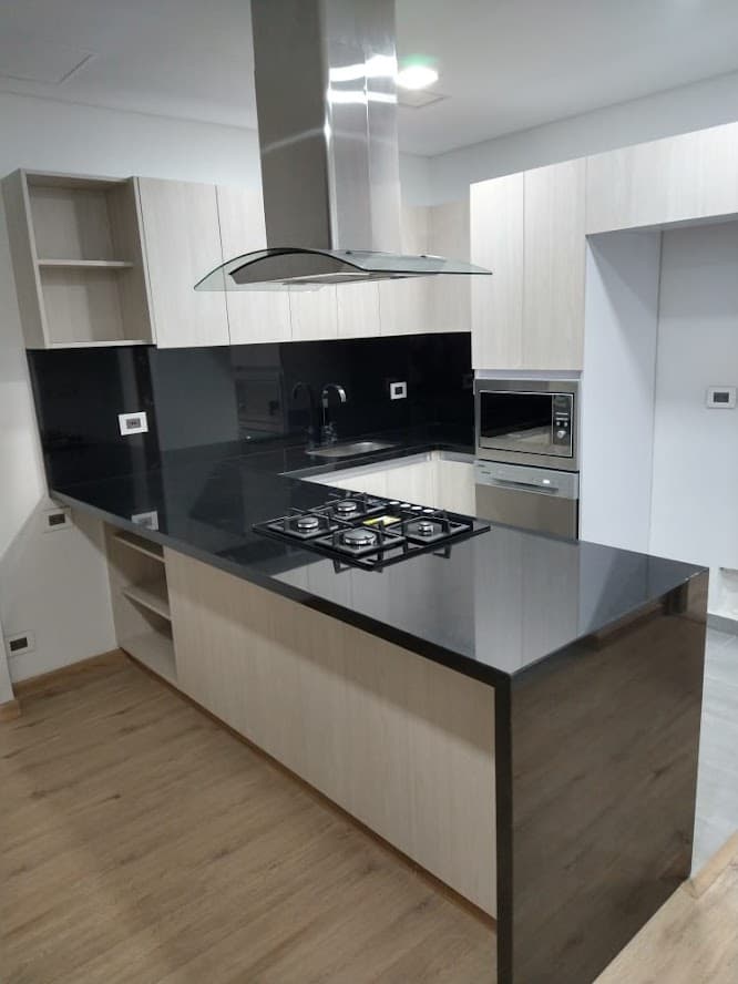 Cocina terminada con mesón de piedra negra, revestimiento brillante y muebles de madera